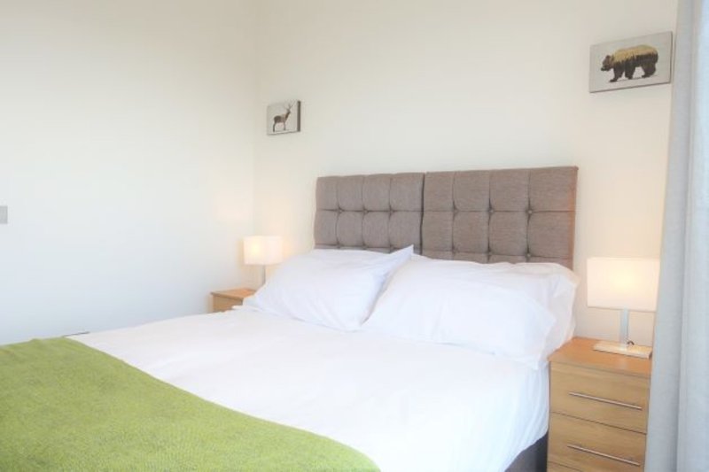 Bedroom with double bed, grey headboard, white bedding, wooden nightstands and lamps