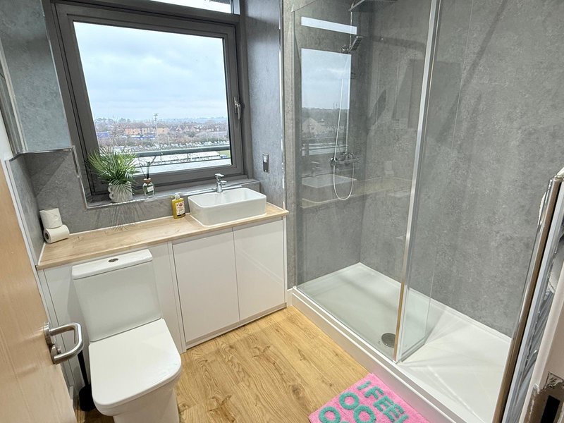 Modern bathroom with vanity, toilet, shower enclosure, wooden flooring and city view window