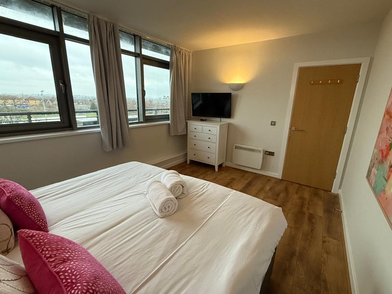 Bright bedroom with double bed, city view windows, wooden floor and TV unit