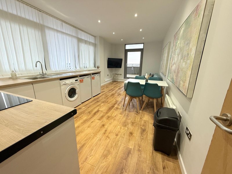 Modern open-plan kitchen and dining area with wooden flooring, white cabinetry, dining table with green chairs