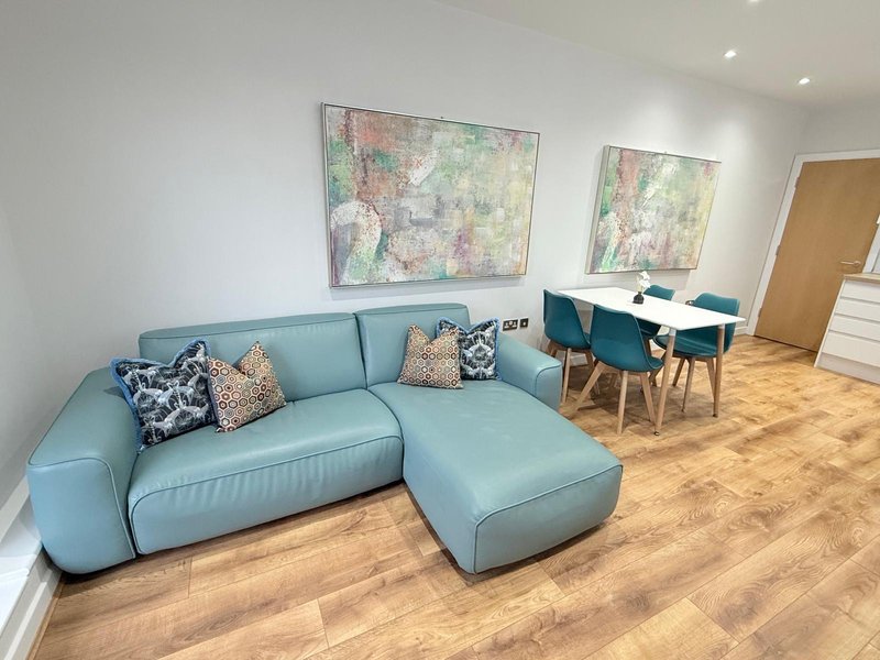 Modern living room with light blue curved sofa, patterned cushions, wooden flooring and wall art