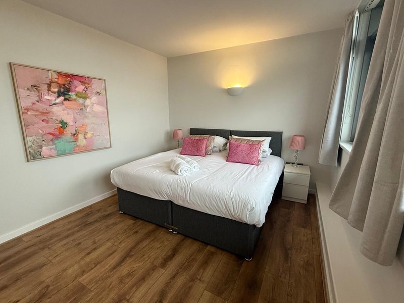 Bedroom with double bed, pink artwork, wooden floor and bedside lamps
