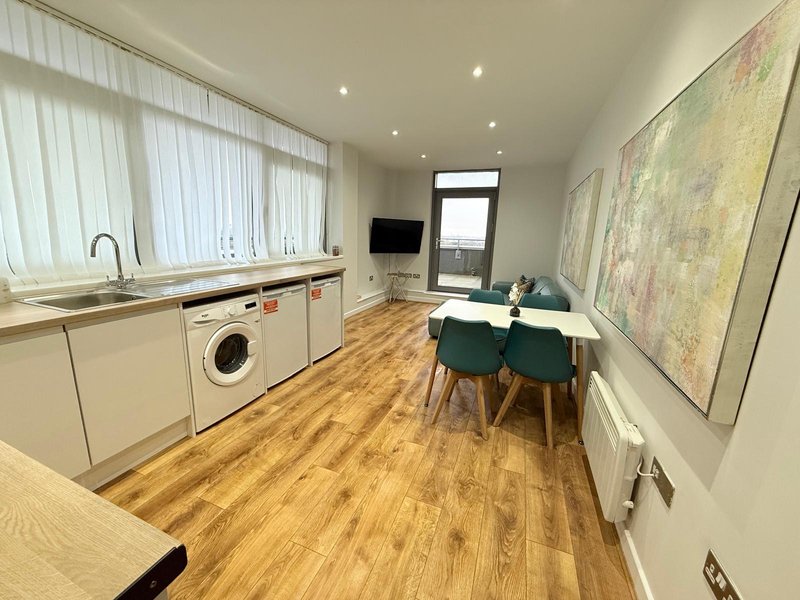 Open-plan kitchen and dining area with white cabinets, wooden flooring, and green dining chairs