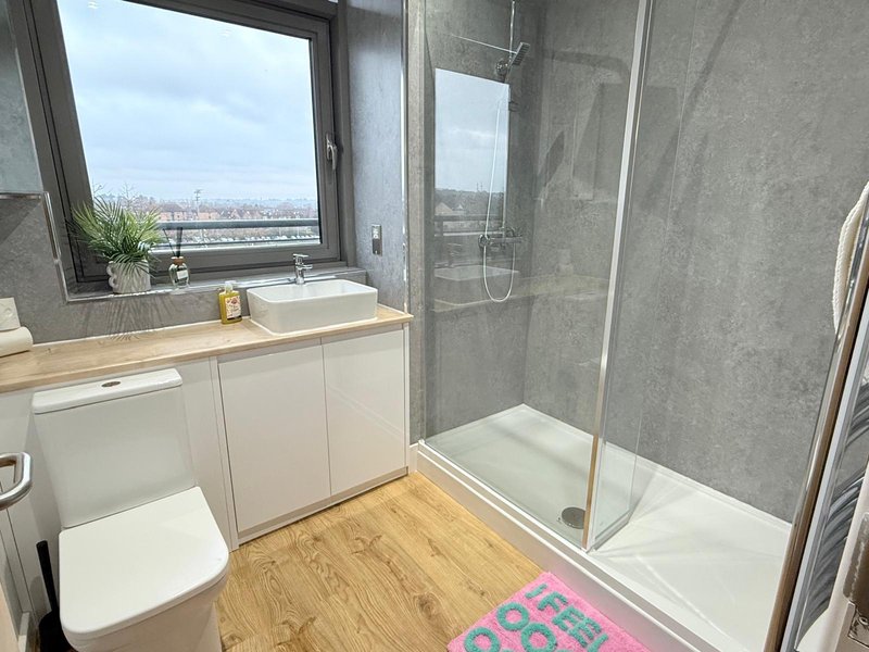 Modern bathroom with white vanity, grey tile walls, shower enclosure, and city view window