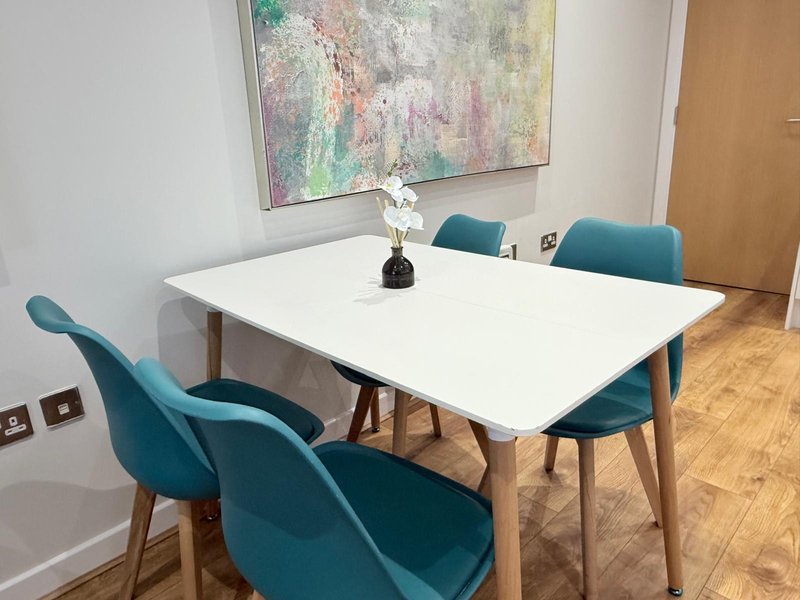Dining room with white table, four teal chairs, framed abstract art, wooden floor