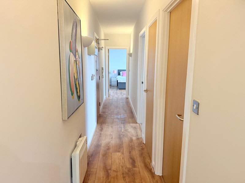 Bright hallway with wooden flooring, white walls, multiple doors, and framed artwork