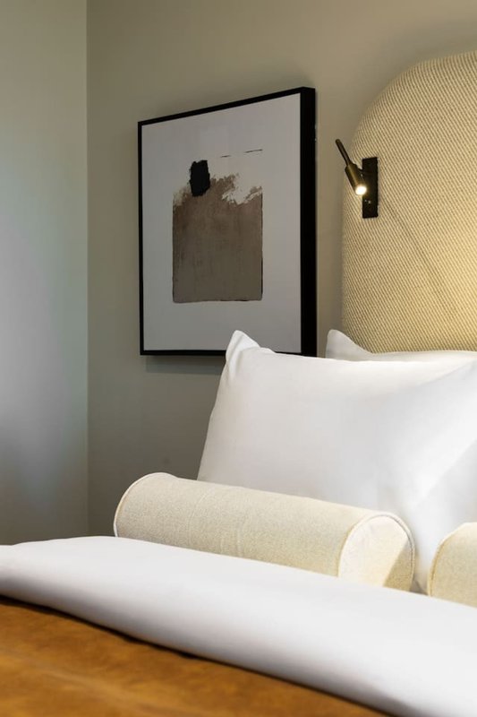 Bedroom with white pillows, beige headboard, framed wall art, and wooden floor