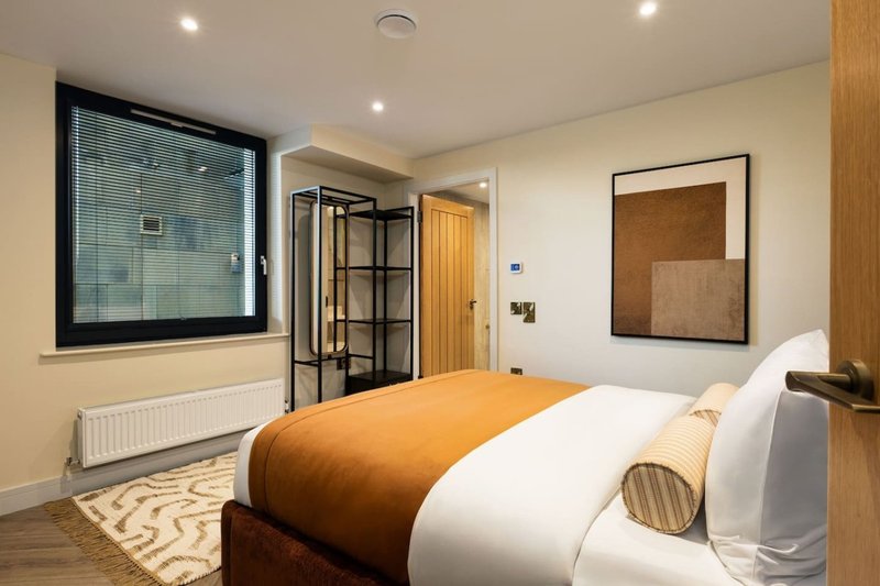 Modern bedroom with double bed, orange and white bedding, ensuite bathroom and framed wall art