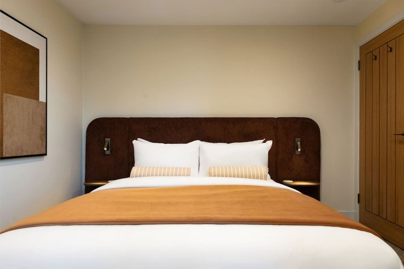 Modern bedroom with dark wood bed frame, white pillows, and orange bedding