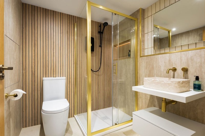 Modern bathroom with white toilet, walk-in shower, dual vanity sink, and gold-framed mirror