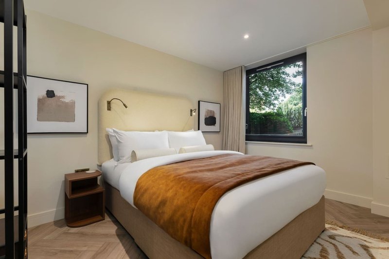 Modern bedroom with double bed, tan leather bench throw, framed wall art and window with garden view