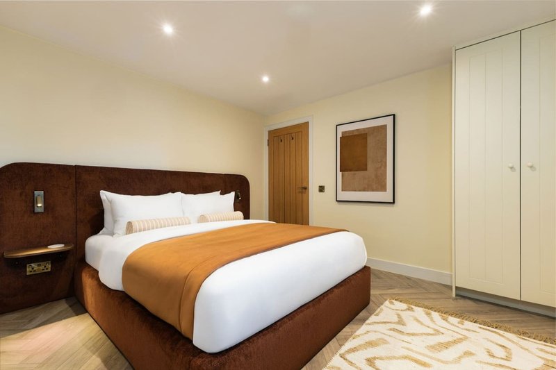 Modern bedroom with brown upholstered bed, white pillows, orange throw, wooden door and fitted wardrobes