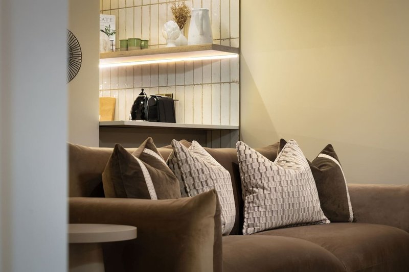 Brown upholstered sofa with neutral cushions and wall-mounted shelving above