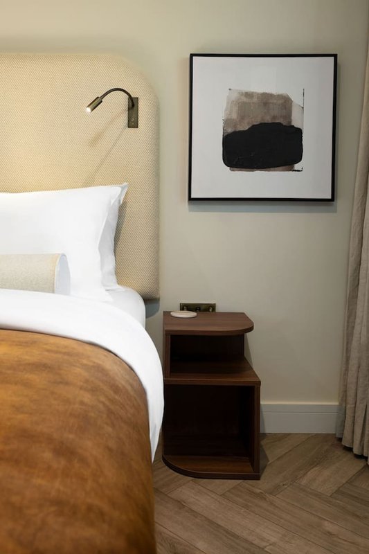 Bedroom with double bed, wooden nightstand, wall-mounted reading lamp and framed artwork