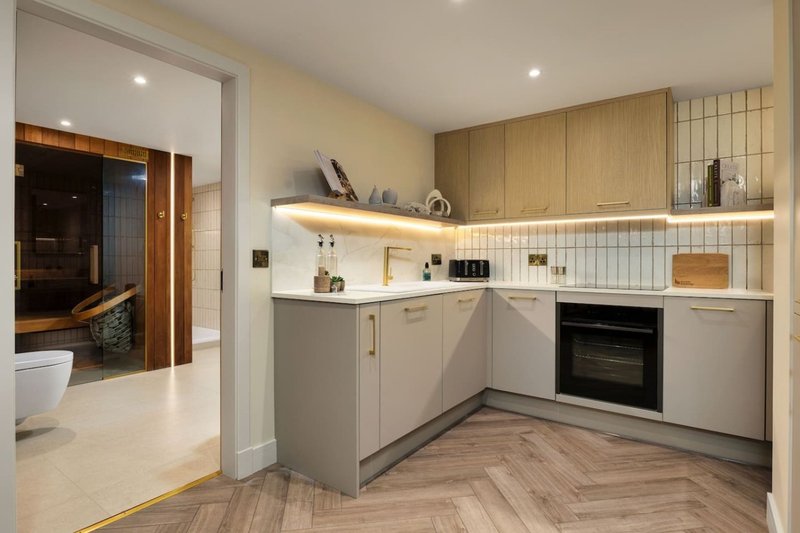 Modern kitchen with grey cabinetry, wooden upper shelving, built-in oven, and herringbone flooring