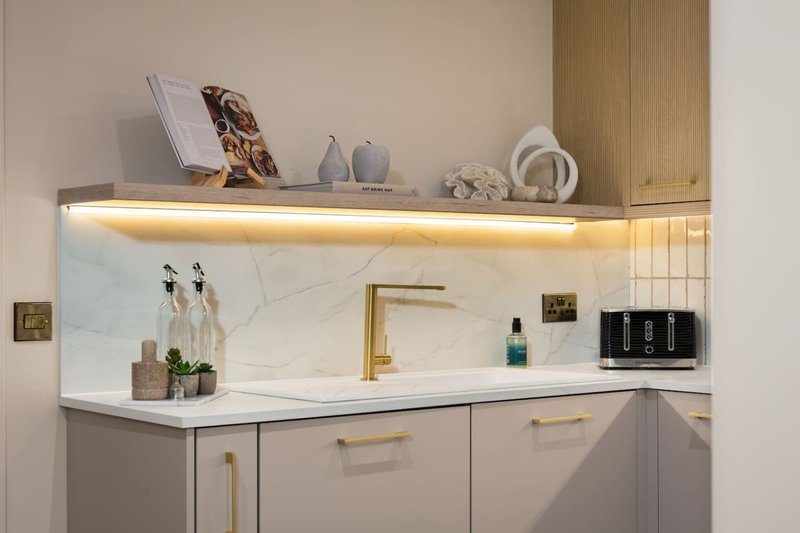 Modern bathroom vanity with marble backsplash, brass faucet, and illuminated shelf above
