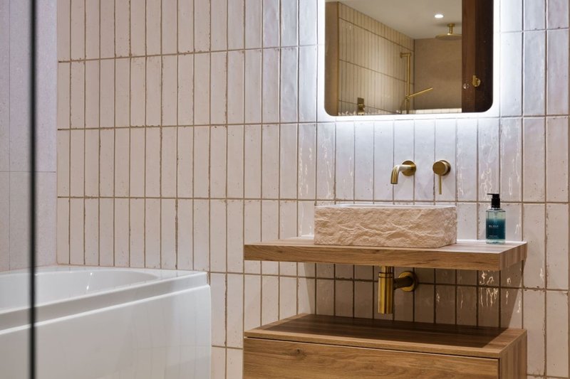 Modern bathroom with white vertical tile, wooden vanity, stone sink and brass fixtures