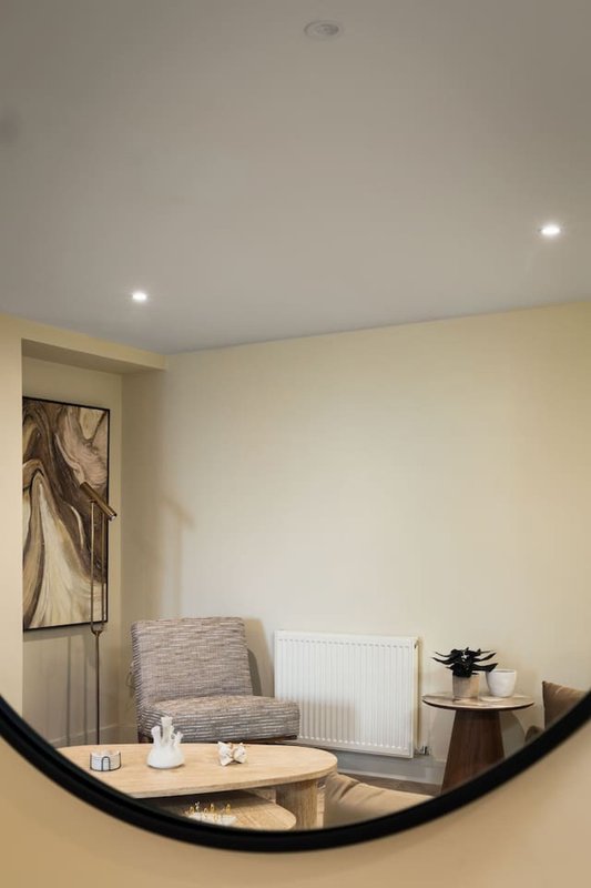 Bedroom corner with upholstered chair, wooden side table, radiator and framed wall art