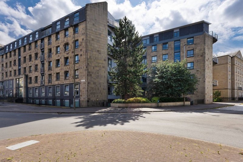 Stone apartment building with multiple floors, tree in courtyard, and paved plaza area