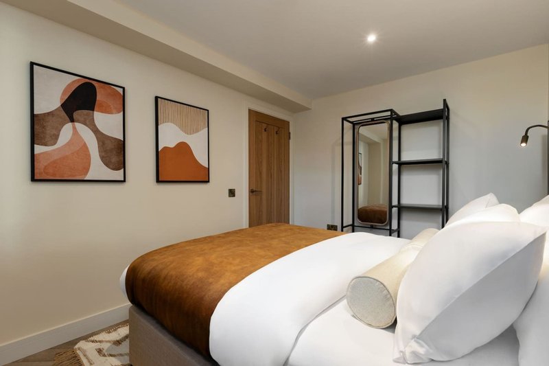Modern bedroom with double bed, white pillows, brown throw, framed abstract wall art and black shelving unit