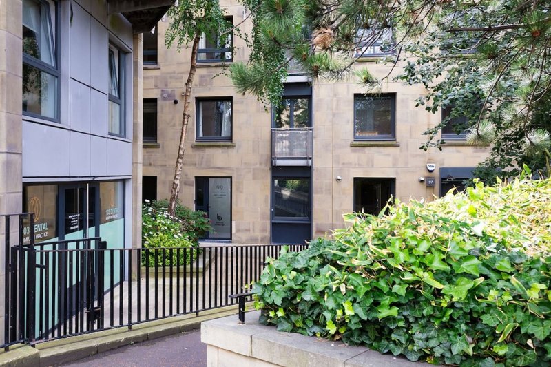 Modern apartment building exterior with black railings, ivy-covered walls, and green landscaping
