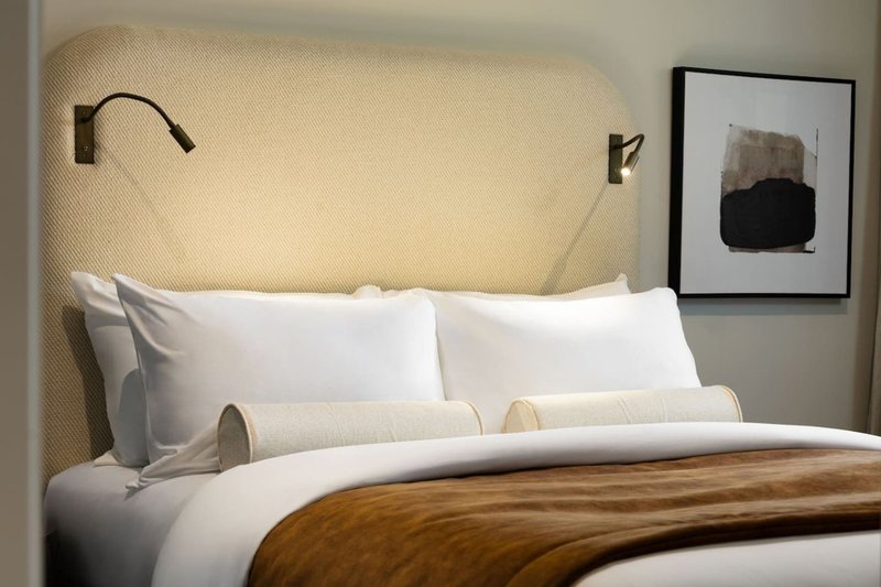 Modern bedroom with cream upholstered headboard, white bedding, wooden throw, and wall sconces