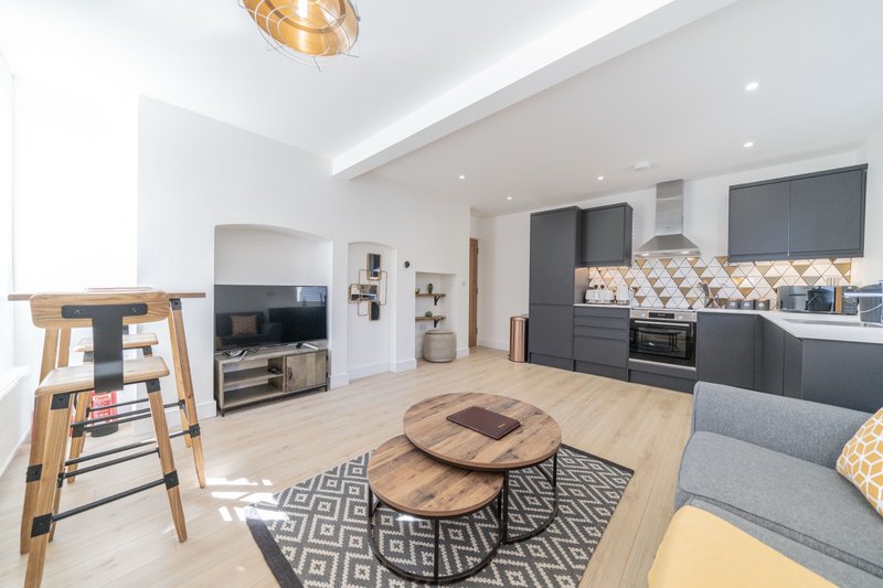 Open-plan kitchen and living area with dark cabinetry, wooden dining table, and grey seating
