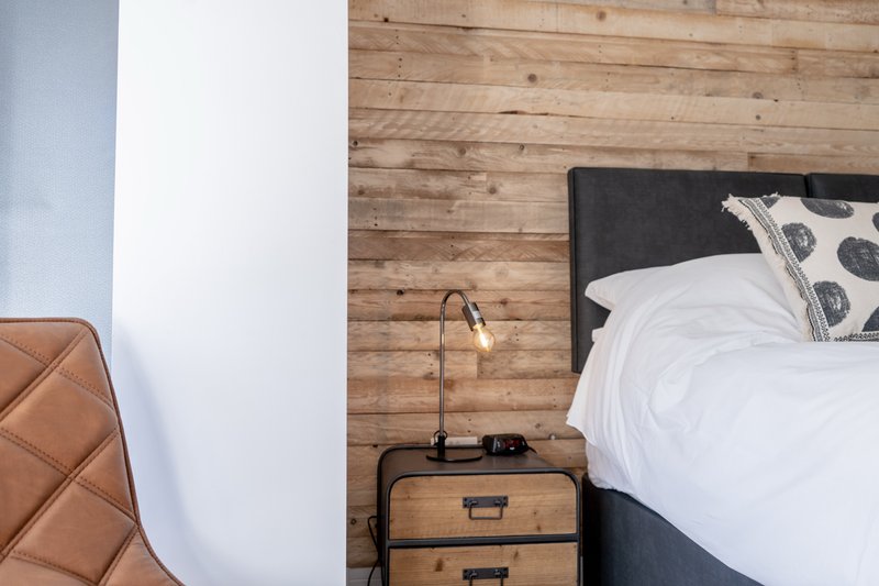Modern bedroom with wooden wall, bed with white bedding, black headboard, and wooden nightstand with lamp