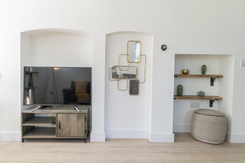 Modern living room with TV stand, wall shelving, decorative mirror, and woven poufs