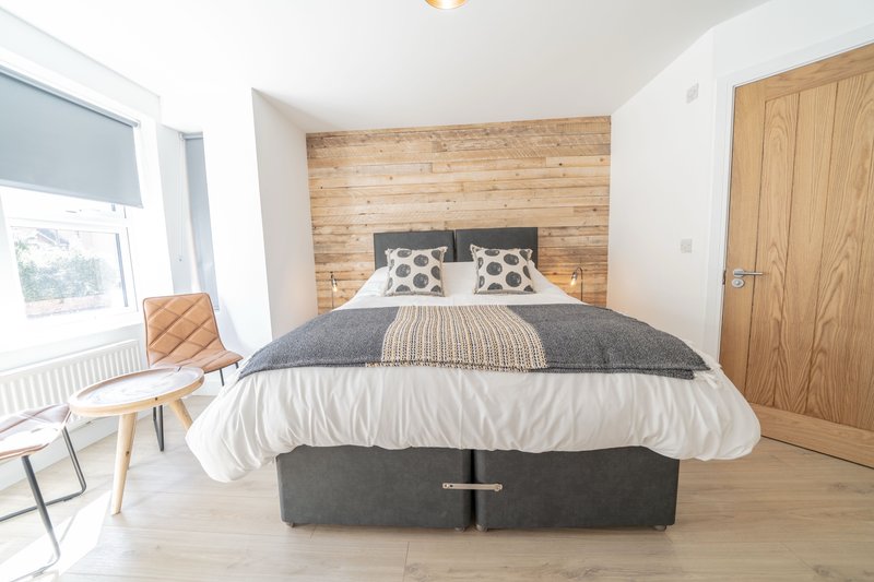 Modern bedroom with double bed, wooden headboard, patterned pillows and natural light