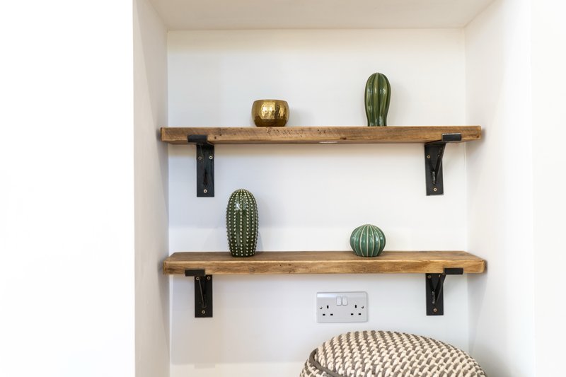 Two wooden shelves with potted cacti and gold decorative bowl above woven pouf