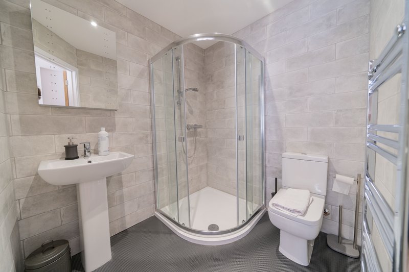 Modern bathroom with curved shower enclosure, pedestal sink, toilet and heated towel rail