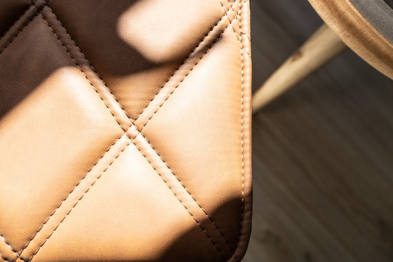 Close-up detail of tan quilted leather bag with stitching and handles