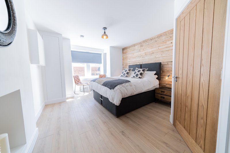 Spacious bedroom with double bed, wooden wall paneling, light wood flooring and access to balcony