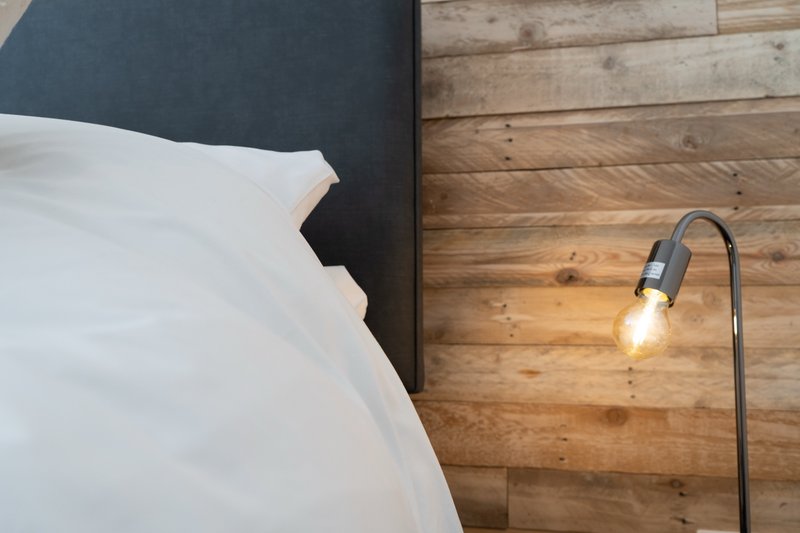 Bedroom corner with white pillows, dark headboard, wooden wall paneling and curved floor lamp