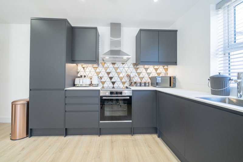 Modern kitchen with dark grey cabinetry, geometric tile backsplash, built-in oven and wooden flooring