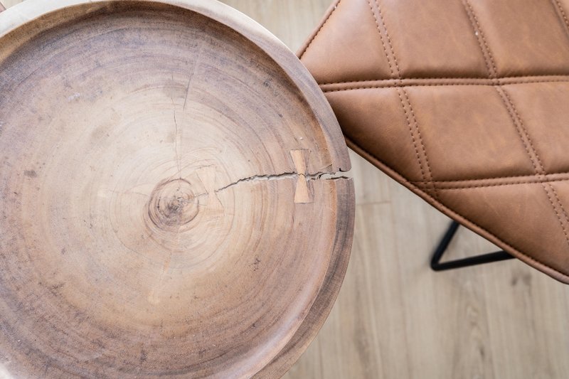 Wooden cross-section slice and tan leather cushion on light wood surface