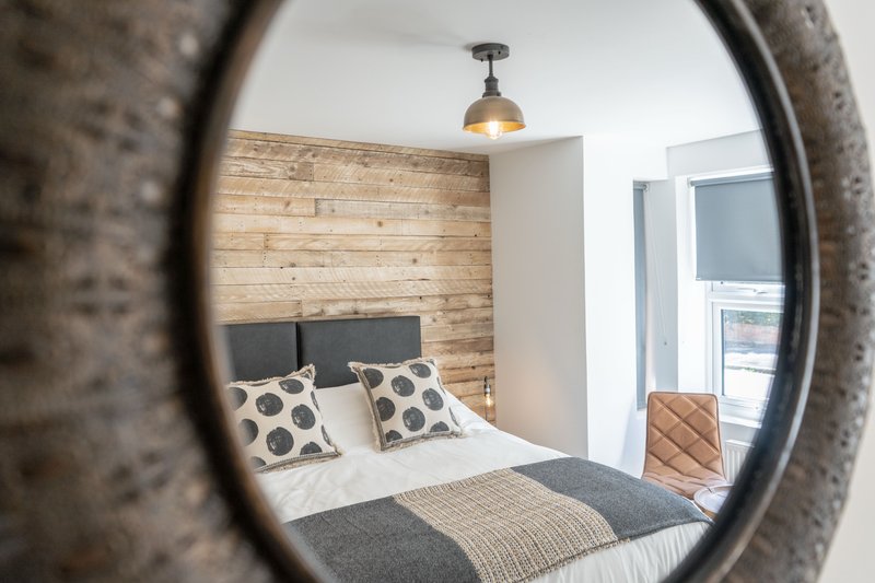 Bedroom viewed through round mirror, with wooden accent wall, double bed and pendant light