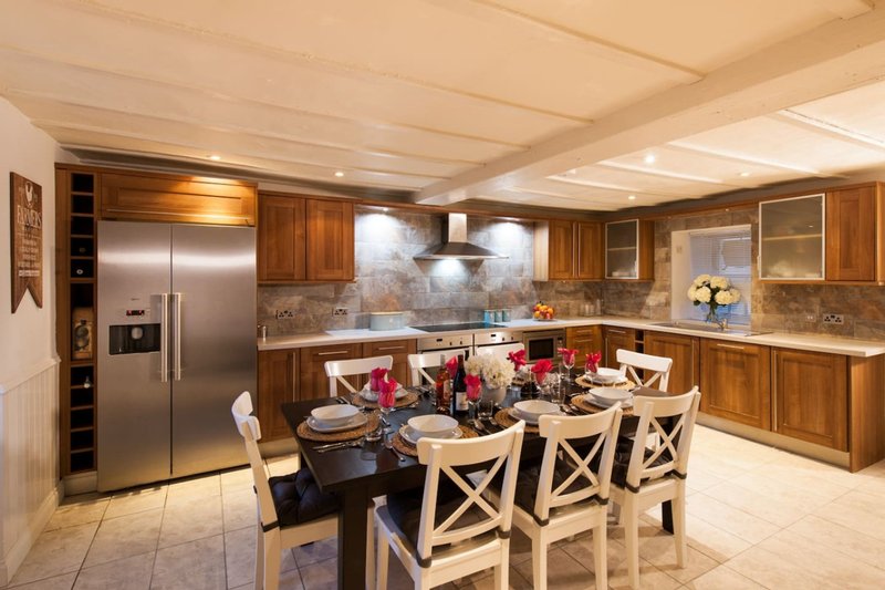 Modern kitchen with wooden cabinetry, stainless steel appliances, island with dining chairs and floral centerpiece