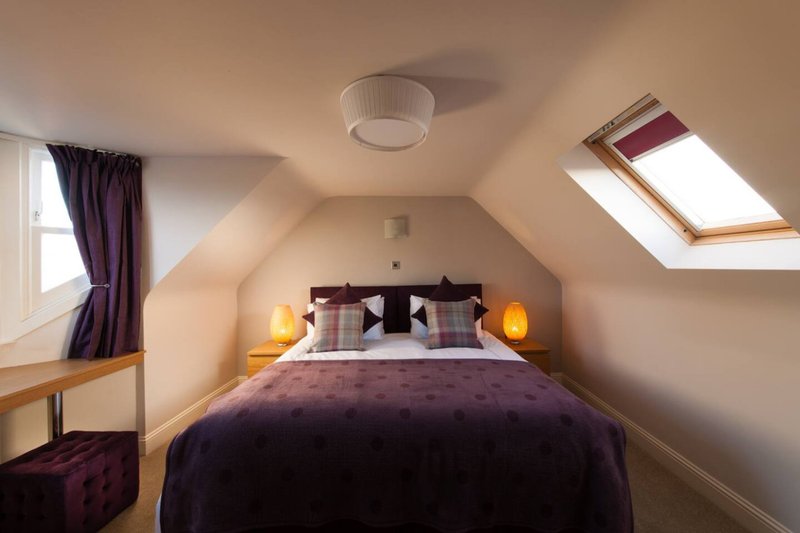 Attic bedroom with double bed, purple bedding, skylights, and warm ceiling lights