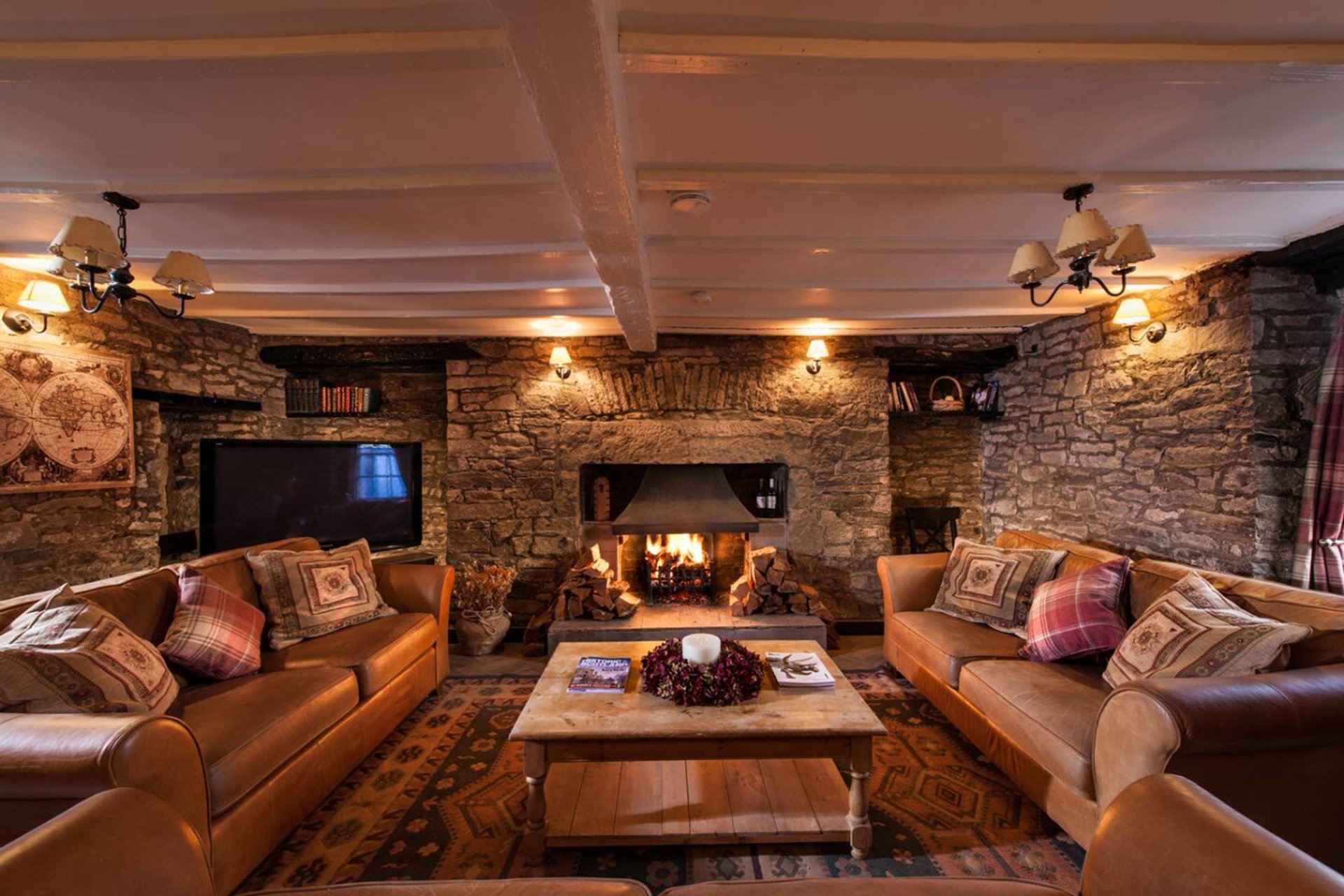 Stone-walled lounge with two leather sofas, fireplace, wooden beams and ambient lighting