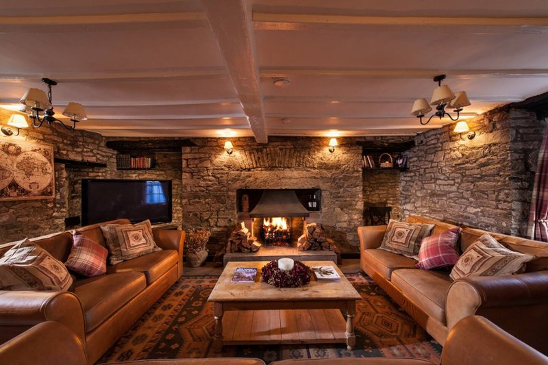 Stone-walled lounge with two leather sofas, fireplace, wooden beams and ambient lighting