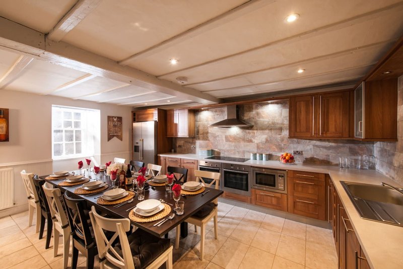 Open-plan kitchen-diner with wooden cabinetry, dining table set for six, and cream tile flooring