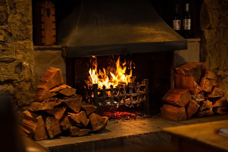 Rustic fireplace with active fire and stacked firewood on stone floor