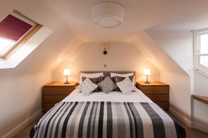 Attic bedroom with double bed, striped duvet, wooden nightstands and warm lighting