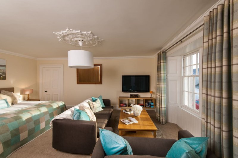 Spacious studio apartment with bed, seating area, TV, and large windows with curtains