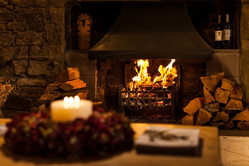 Cozy fireplace with active fire, stacked firewood, candles and flowers in foreground