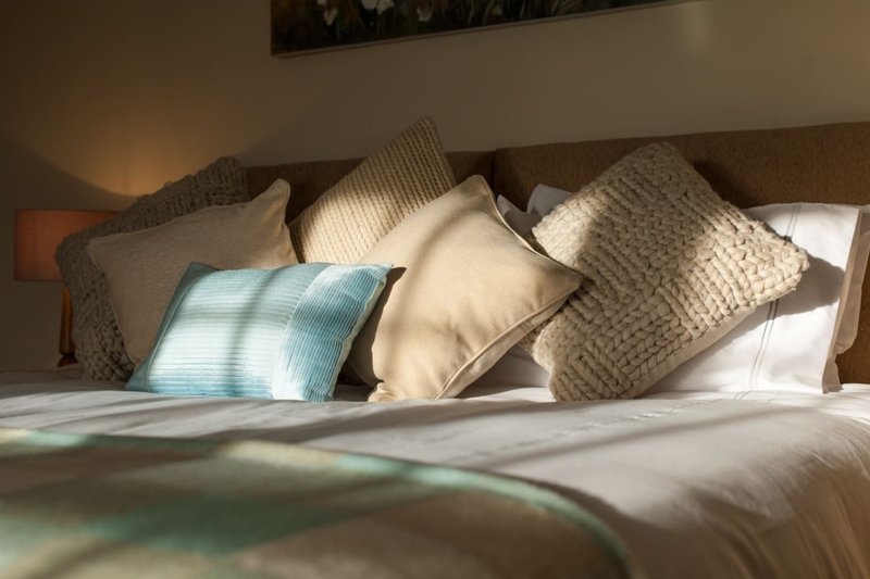 Bedroom with neatly arranged pillows and cushions on made bed against headboard