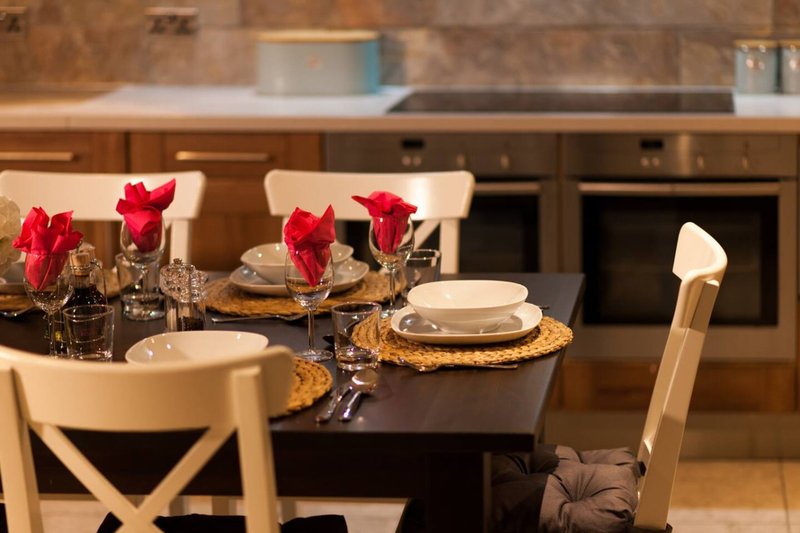 Dining table set with red flowers, place settings, and kitchen visible in background