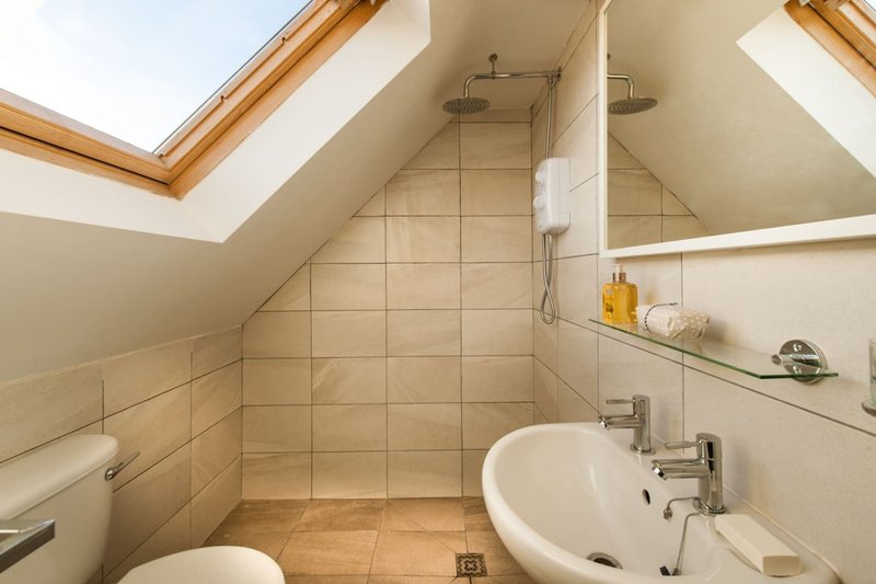 Bathroom with double sink, toilet, shower enclosure, skylight and beige tile walls